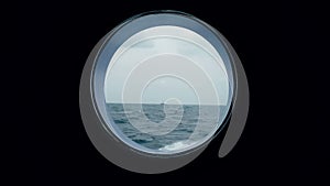 View of the ocean from the porthole of the ship going. A ship in the ocean is visible from the porthole of a cruise