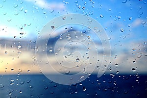 View of the ocean and sky through raindrops on the glass of a ship`s porthole.