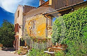 View on ochre natural stone farm house in provence style with lush green garden, blue sky - Roussillon, France