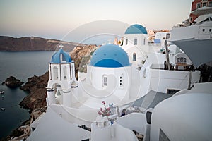 View of Oia white washed buildings with the famous three blue domes church taken at sunrise