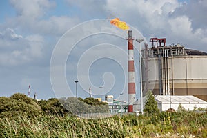 View of oil refinery plant with its flaming fireplace against blue sky