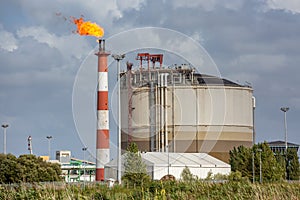 View of oil refinery plant with its flaming fireplace against blue sky