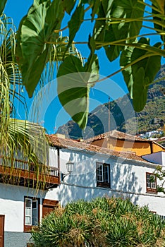 View on old authentic spanish building behind the tropical plants. Mountains and blue sky on the background.