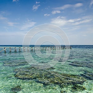 View of old broken jetty during sunny day with coral and green s