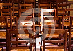 View on  old brown wood chairs with backrest in a row inside catholic empty church illuminated by natural sun light