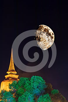 A view of an old Buddhist stupa illuminated in golden light with a huge moon