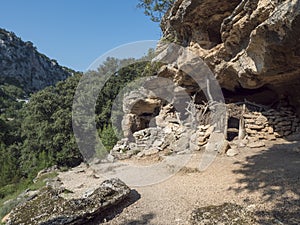 View of old cave shepard shelter on hiking path to Cala Goloritze beach with limestone rocks, trees, green bush. Gulf of Orosei,