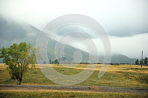 View of the old farm fence at the foot of a high mountain range covered with thick fog