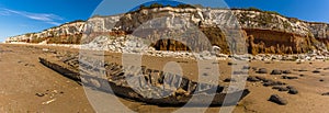 A view of Old Hunstanton Beach showing a shipwreck, chalk rockfalls and white, red and orange stratified cliffs in Norfolk, UK