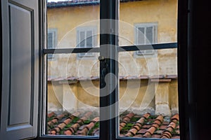 View from an old Italian window with wooden shutters on a tiled roof and a wall with windows