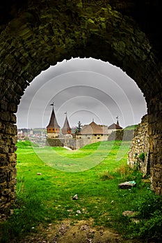 View of the Old Kamyanets-Podilsky castle from under an old arch under a cloudy gray sky. The fortress is located amidst