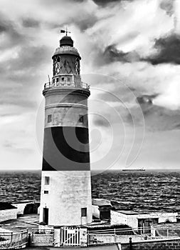 View of old lighthouse on background cloudy sky. Black and white image