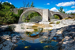 View of an old stone arch bridge over a dried river on a clear sky background
