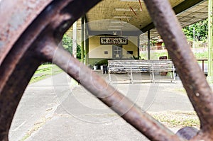 View of the old train station Atenas, through the spokes of an old rusty railway wheel