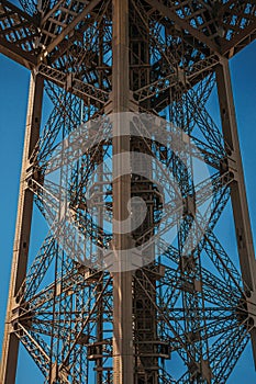 View of one legâ€™s iron structure of the Eiffel Tower, with sunny blue sky in Paris.