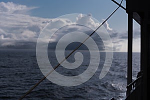 A view of the open, deep blue sea from the railing of a passenger ship - in the background you can see how a storm