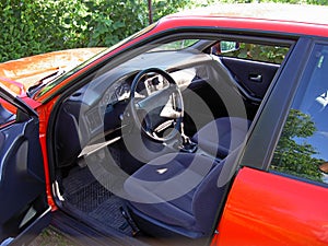 View through the open door to the red car from the left, from the driver`s side