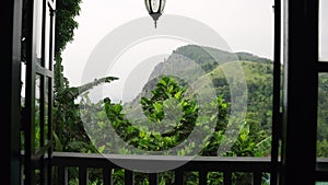 View from open terrace, rich plants surrounds scenic Ella Rock. Balcony rail in foreground, tranquil Sri Lankan