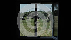 View from an open window with a transparent curtain swinging in the wind on a rural landscape with a meadow and wooden