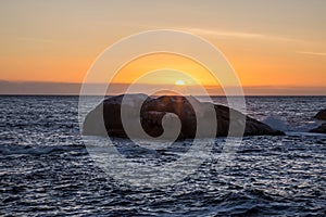 View of orange sunset over ocean with big rock