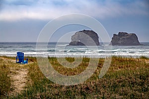 View of the Oregon Coast with it`s sandy beaches, sea stacks and ocean waves. Blue lounge chair on the shore, loneliness.