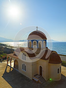 View of orthodox greek church at mediterranean coast. Orange foof, white building and blue sea waves. Crete island