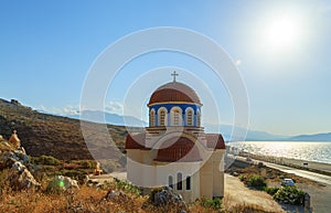 View of orthodox greek church at mediterranean coast. Orange foof, white building and blue sea waves. Crete island
