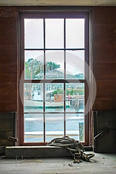 View out dirty grungy paned window on rainy day from workshop building with rope laying on a shelf to other marina buildings and