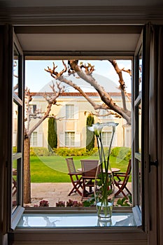 View out of opened window with vase on sill to backyard with patio, formal garden of Chateau Cordeillan-Bages, Bordeaux, France.