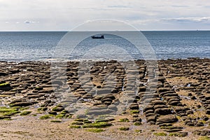 A view out to sea towards tourist boats offshore across the sea eroded boulders on the beach at Old Hunstanton, Norfolk, UK