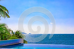 View of the outdoor pool by the sea. There is a lush palm tree next to the pool. Sanya, China.