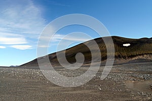 View over barren waste land on black hill with  white spot of melted snow contrasting with blue sky, Iceland