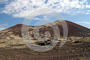 View over barren wide plain on red and green bare hills contrasting with blue sky and cumulus clouds - Iceland