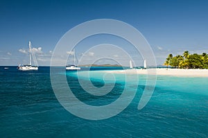 View over beautiful bay to palms and beach of Palm Island. White sand, turquoise sea, boats on water and blue sky.