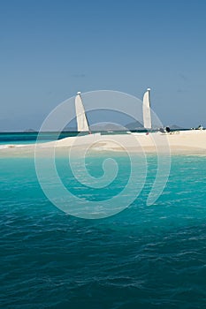 View over beautiful bay to palms and beach of Palm Island. White sand, turquoise sea, boats on water and blue sky.