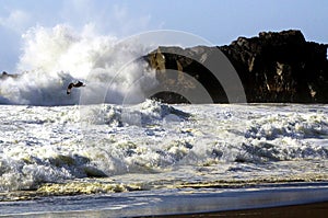 View over black lava sand beach and white furious foaming water surf on wave which breaks against rock photo