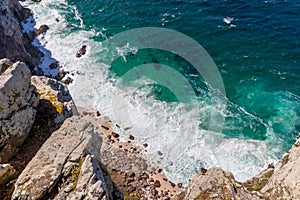 View over the cliffs at the deep ocean and waves swirling at small beach and rocks at Cape Point South Africa