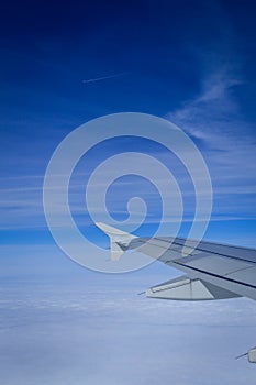 View over the clouds from the porthole of an airplane with plane wing