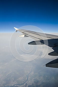 View over the clouds from the porthole of an airplane with plane wing