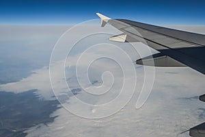 View over the clouds from the porthole of an airplane with plane wing