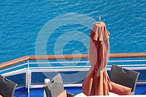 View over cruise ship deck to ocean with outdoor dining furniture and beach umbrella