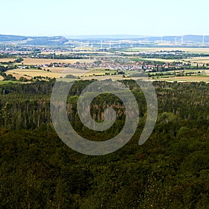 View over the dense green forest in the Harz Mountains to a village near Bad Harzburg with wind turbines in the background