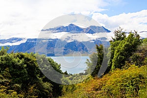 View over green grass and plants on lake with high rugged mountains background. Depp clouds hanging in mountain peak. photo