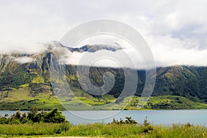 View over green grass and plants on lake with high rugged mountains background. Depp clouds hanging in mountain peak. photo