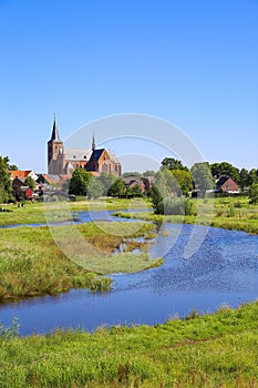 View over green wetland water on cityscape of durch town with tower of medieval church against blue summer sky - Neer Limburg,