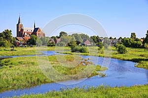 View over green wetland water on cityscape of durch town with tower of medieval church against blue summer sky - Neer Limburg,