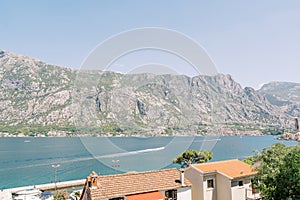 View over the red roofs of houses to a motor boat sailing on the sea against the backdrop of mountains