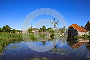View over reflecting river pond on old water mill restaurant against deep blue cloudless summer sky - Neer Limburg, Netherlands