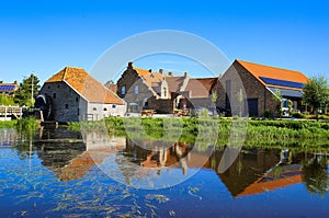 View over reflecting river pond on old water mill restaurant against deep blue cloudless summer sky - Neer Limburg, Netherlands