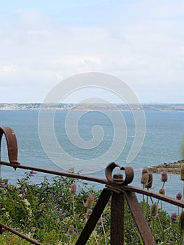 View over a rusty railing from Moushole to the blue sea of the Cornish coast and Saint Michael's Mount Cornwall England